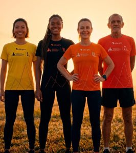 Quatro corredores exibem as camisetas oficiais da Maratona Internacional de Maringá em campo aberto ao pôr do sol