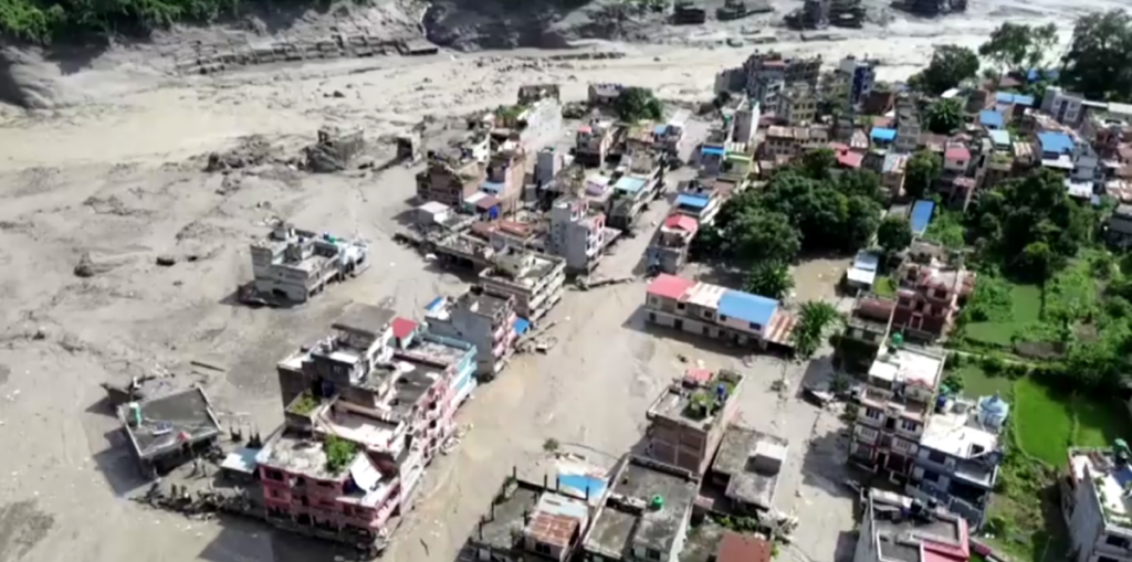 Vista aérea de área devastada com edifícios danificados e terreno arrasado após desastre natural