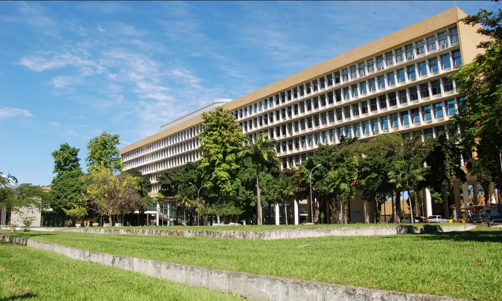 Prédio da UFRJ com fachada ampla e jardim verde sob céu azul claro