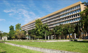 Prédio da UFRJ com fachada ampla e jardim verde sob céu azul claro