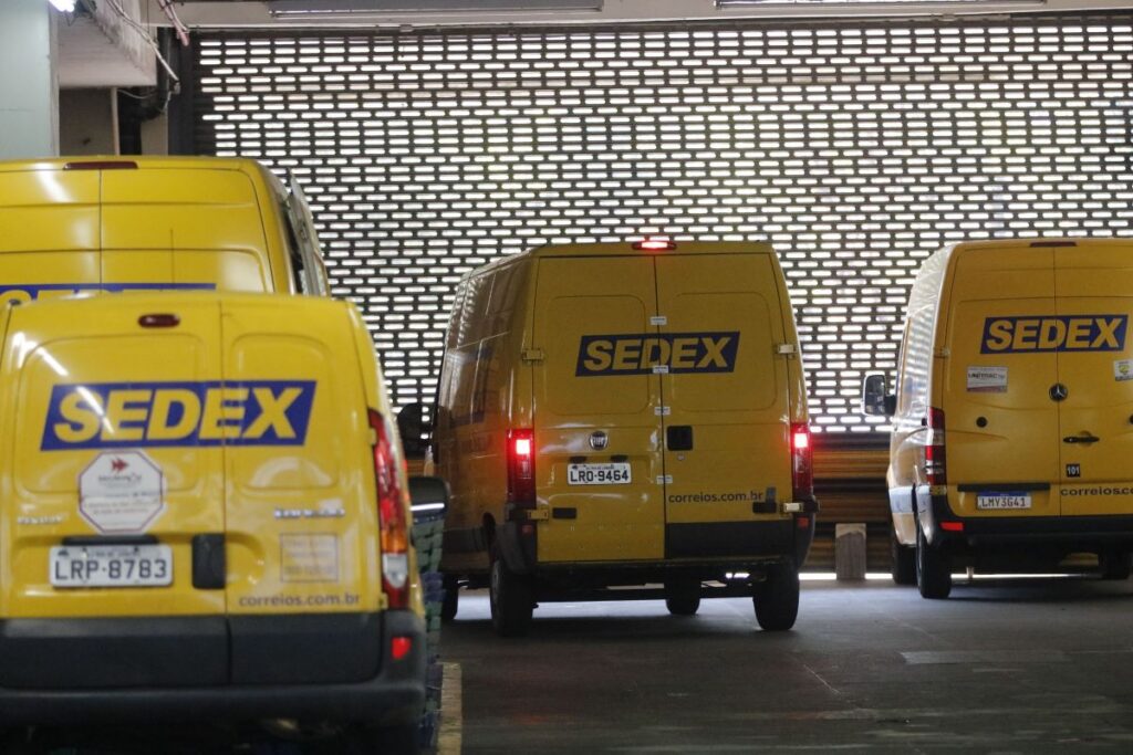 Frotas de caminhões amarelos do Sedex estacionados em pátio interno de centro de distribuição
