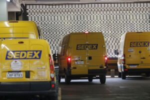 Frotas de caminhões amarelos do Sedex estacionados em pátio interno de centro de distribuição
