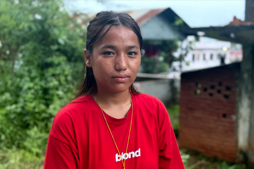Jovem com expressão séria em meio a cenário de comunidade afetada por enchentes no Nepal