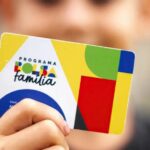 Mão segura cartão do Programa Bolsa Família com design colorido em destaque