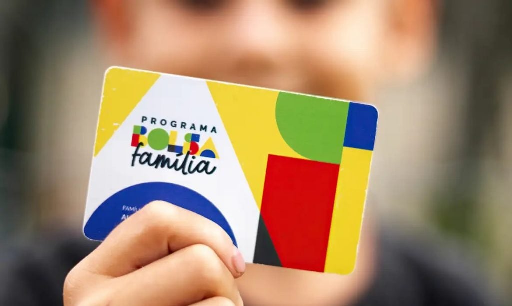 Mão segura cartão do Programa Bolsa Família com design colorido em destaque
