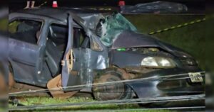 Carro destruído após colisão com poste à noite, com destaque para danos na frente e laterais