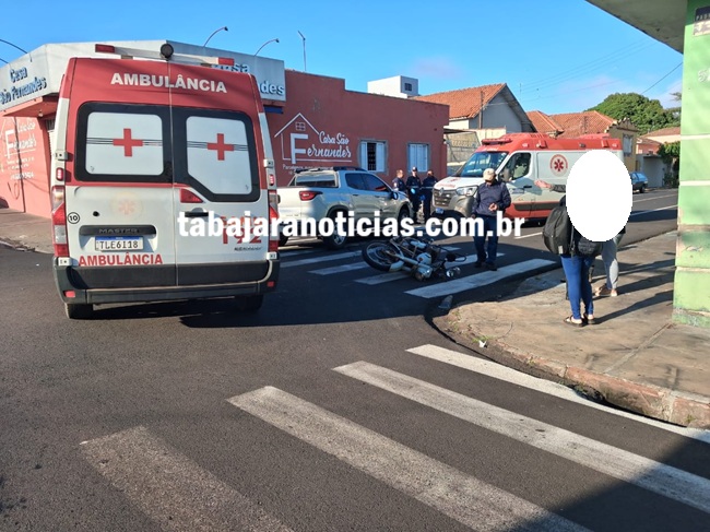 Motocicleta tombada em faixa de pedestres com ambulâncias e pessoas próximas ao local do acidente