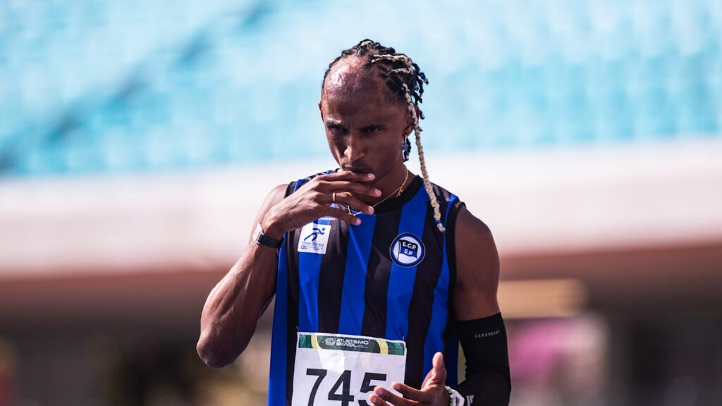 Um atleta com uniforme listrado azul e preto e número 745 em um estádio, com ar concentrado