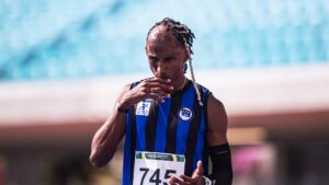Um atleta com uniforme listrado azul e preto e número 745 em um estádio, com ar concentrado