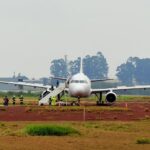 Avião comercial parado em pista com equipe de segurança e escada móvel ao lado