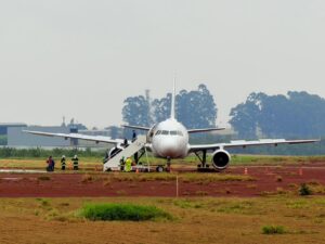Avião comercial parado em pista com equipe de segurança e escada móvel ao lado