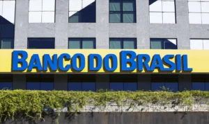 Fachada de um prédio com letreiro amarelo e azul de banco, cercado por vegetação