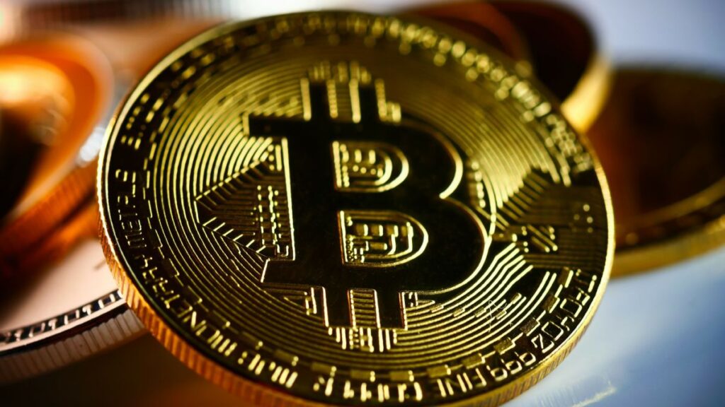 Moeda física com símbolo do Bitcoin em destaque sobre outras moedas douradas