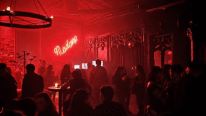 Interior de boate com iluminação vermelha e letreiro neon "Madame", com pessoas circulando e conversando