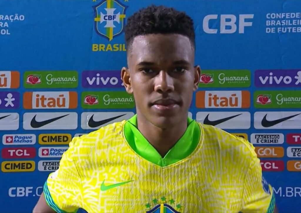 Um jovem atleta com camisa amarela da seleção brasileira em frente a painel da CBF com patrocinadores