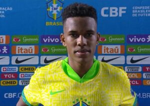 Um jovem atleta com camisa amarela da seleção brasileira em frente a painel da CBF com patrocinadores
