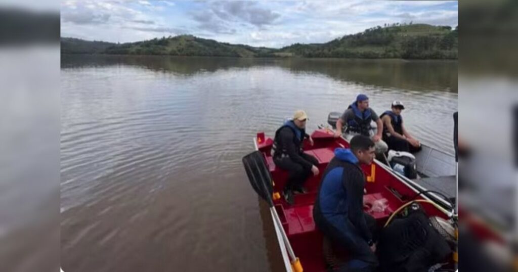 Quatro homens em barco vermelho navegam por represa cercada por colinas arborizadas
