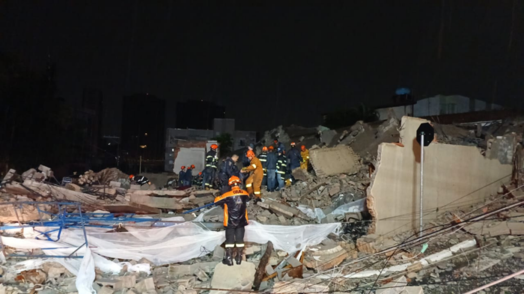 Um grupo de resgatistas trabalha entre escombros de edifício desabado à noite