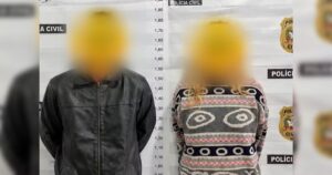 Um homem e uma mulher em frente a parede de medição da Polícia Civil com rostos pixelados
