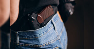 Pessoa com pistola presa na cintura, parcialmente visível sob camiseta e calça jeans