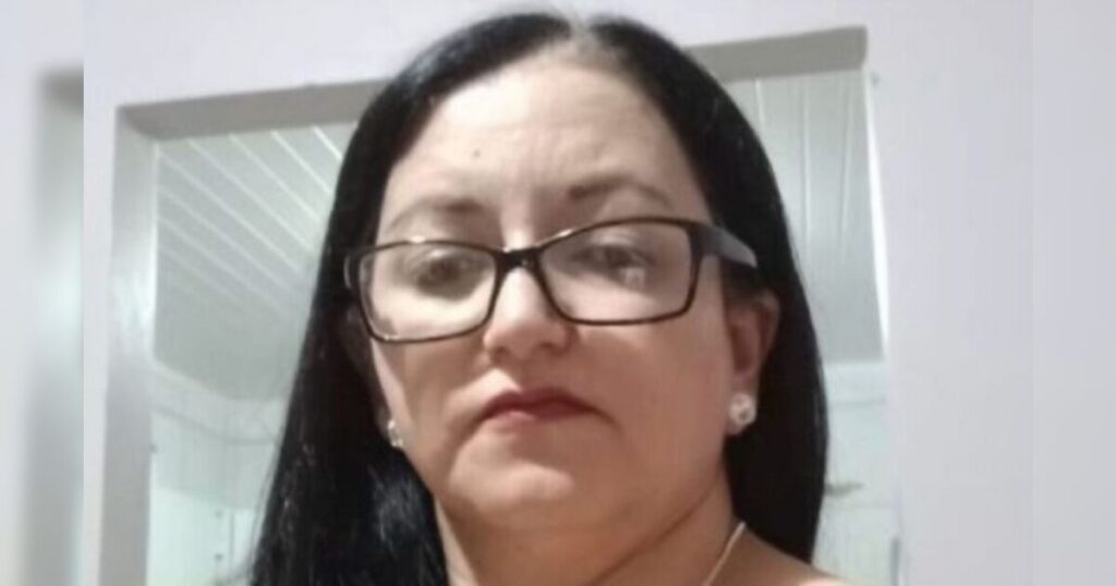 Mulher de cabelos escuros e óculos olha para a câmera em ambiente interno