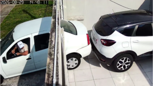 Um homem dentro de uma van branca com o braço para fora, próximo a dois carros estacionados em área externa