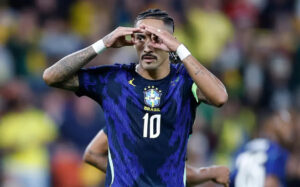Um jogador com camisa da seleção brasileira faz gesto com as mãos em campo