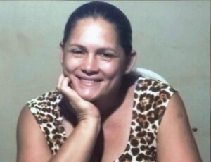 Uma mulher sorrindo com a mão no rosto, vestindo blusa estampada em fundo claro