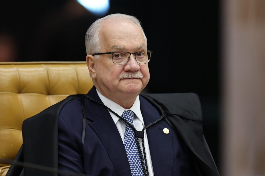 Um homem de terno e toga sentado em uma cadeira dourada em ambiente formal