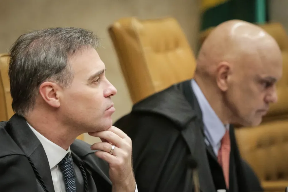 Dois homens de toga sentados em cadeiras de madeira em ambiente formal, um com a mão no queixo