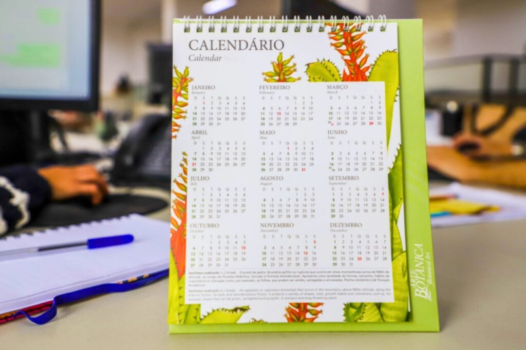 Calendário de mesa com ilustrações botânicas exibindo os meses do ano sobre uma superfície de trabalho
