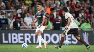 Dois jogadores disputam a bola em campo durante partida da Libertadores com torcida ao fundo