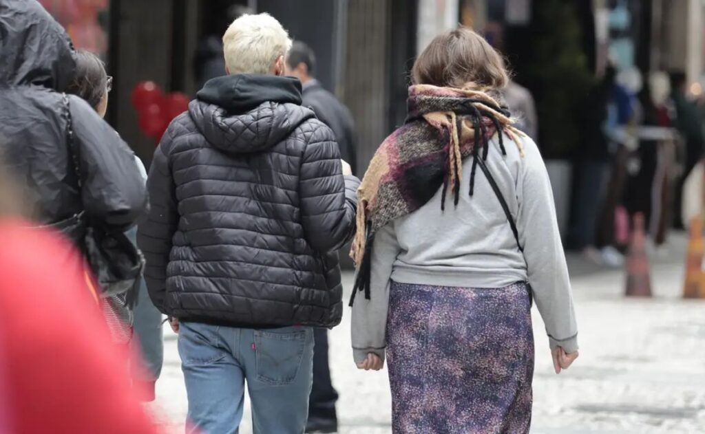 Pessoas caminham por rua com roupas quentes em dia frio