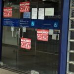 Porta de agência com cartazes vermelhos anunciando greve de bancários
