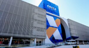 Fachada de um prédio com grande letreiro da Caixa e design moderno em tons de azul, branco e laranja