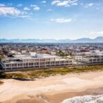 Conjunto de edifícios modernos ao lado de praia com ondas e montanhas ao fundo