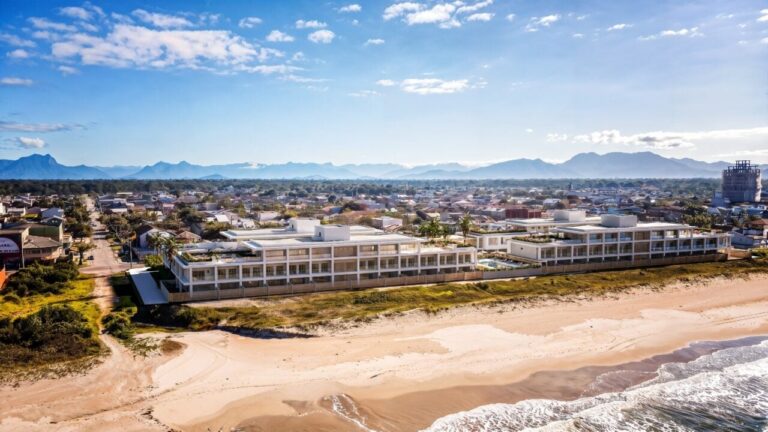 Conjunto de edifícios modernos ao lado de praia com ondas e montanhas ao fundo