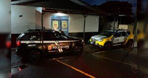 Veículos da Polícia Civil e Polícia Militar estacionados em frente a uma delegacia à noite