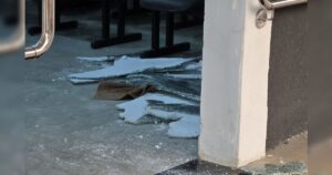 Fragmentos de vidro espalhados no chão de uma área interna com cadeiras e coluna ao fundo
