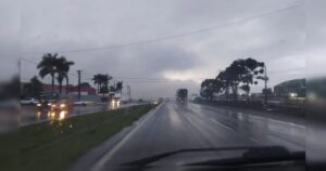 Pista molhada com veículos circulando sob forte chuva e céu nublado
