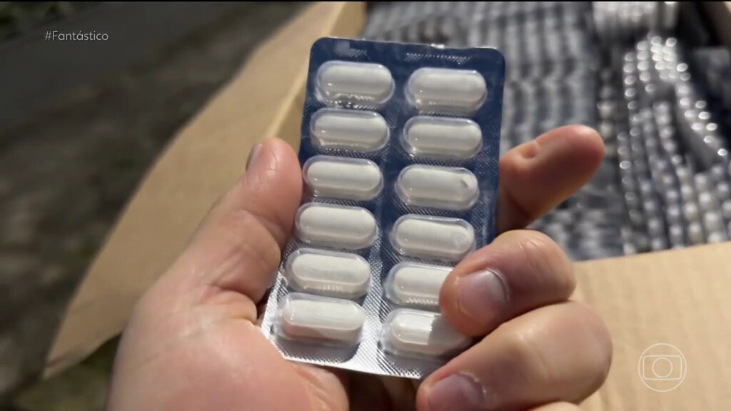 Mão segura blistre com comprimidos brancos em meio a caixas de medicamentos