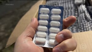 Mão segura blistre com comprimidos brancos em meio a caixas de medicamentos