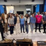Um grupo de pessoas posa em frente a instrumentos musicais em ambiente interno com paredes azuis