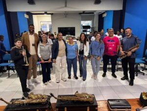Um grupo de pessoas posa em frente a instrumentos musicais em ambiente interno com paredes azuis