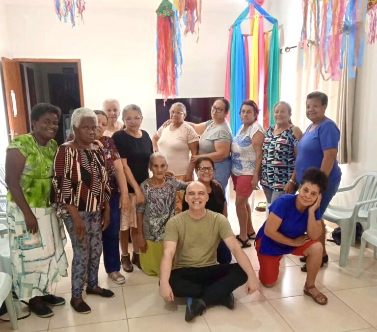 Um grupo de pessoas posa em ambiente decorado com tecidos coloridos, em atividade de teatro para idosos