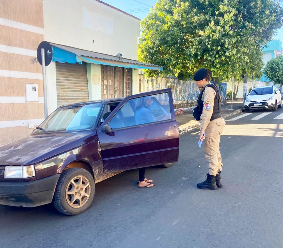 Um agente em uniforme conversa com uma pessoa dentro de um carro estacionado na rua