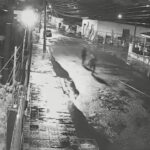Duas pessoas correm por rua molhada em cena noturna captada por câmera de segurança