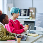 Duas pessoas trabalham em computadores em um ambiente de escritório moderno com código exibido nas telas