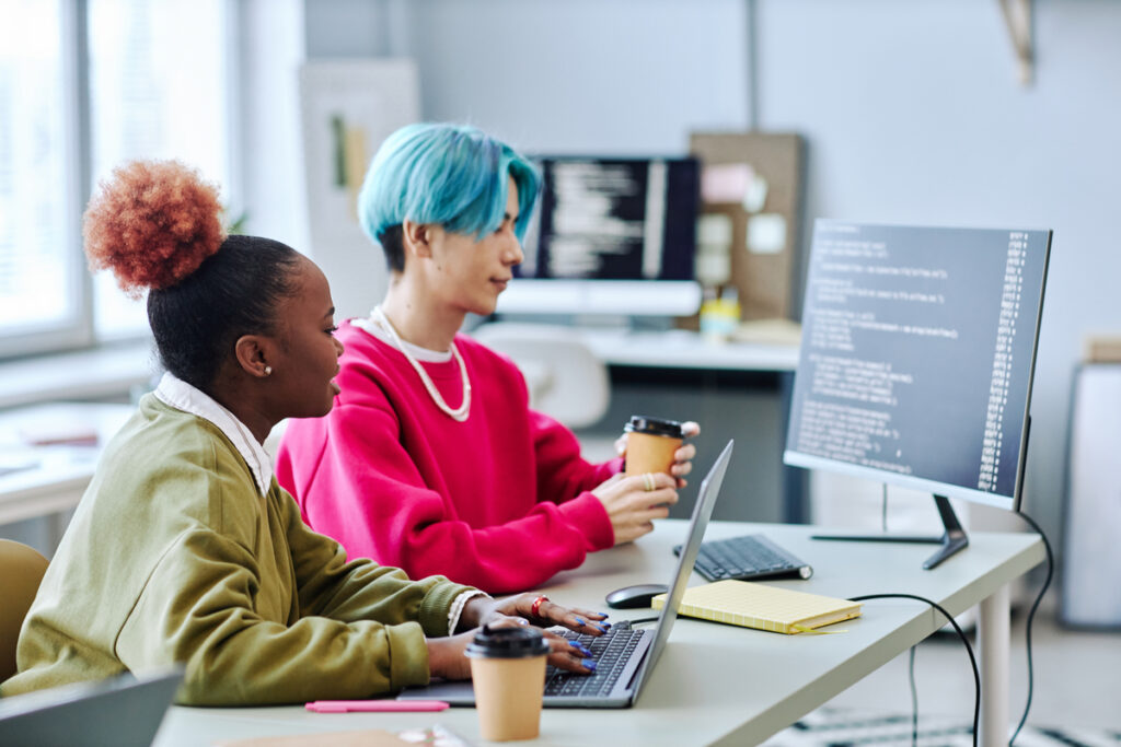 Duas pessoas trabalham em computadores em um ambiente de escritório moderno com código exibido nas telas