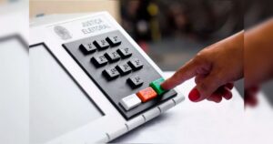 Uma mão pressiona o botão verde em uma urna eleitoral da Justiça Eleitoral